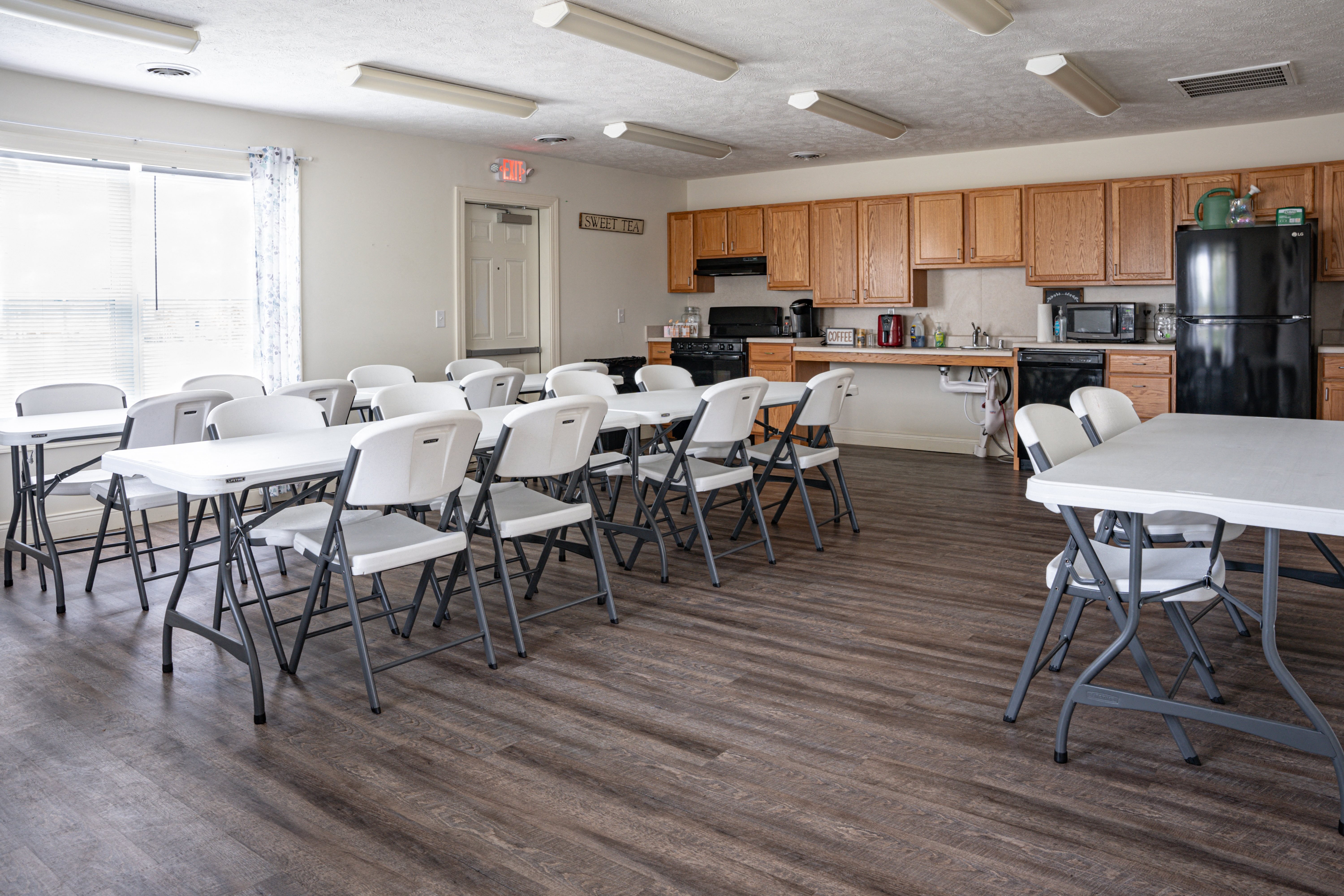 a community room with tables and chairs and a kitchen